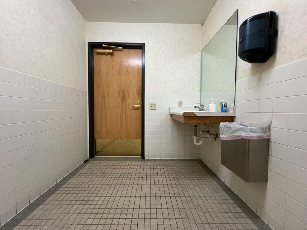 Modern public restroom interior with a handbasin, mirror, and wooden door.